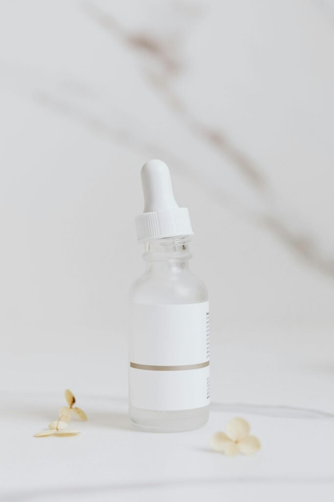 Elegant product photography of a glass serum bottle on a white surface with flowers.